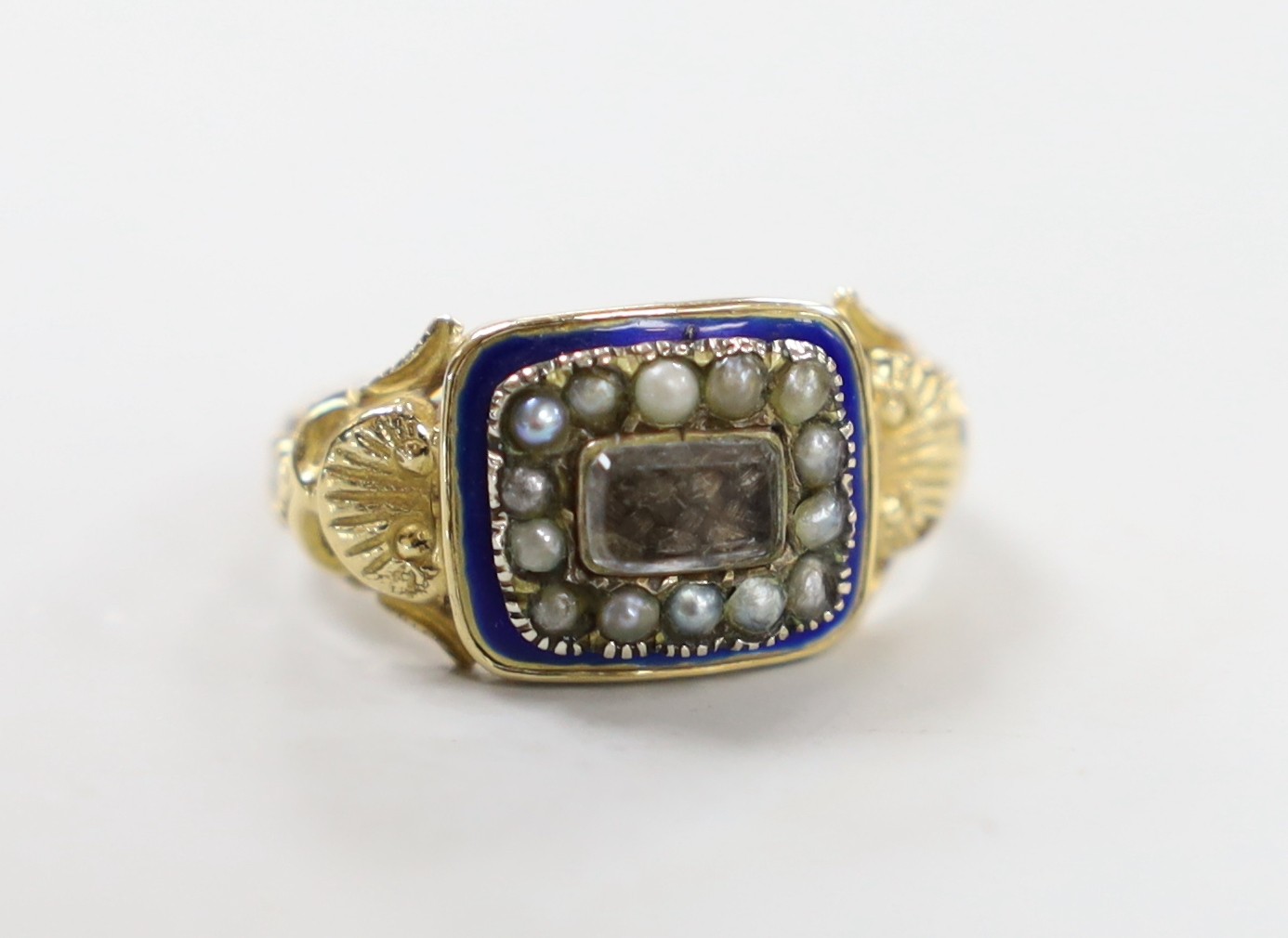 A 19th century yellow metal, enamel, seed pearl and plaited hair set mourning ring, with shell decorated shoulders, size M, gross weight 3 grams.